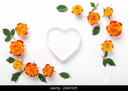 Composizione di fiori. Cornice fatta di fiori di rosa e vaso vuoto a forma di cuore su sfondo bianco. Concetto di giorno di San Valentino. Disposizione piatta, vista dall'alto - immagine Foto Stock