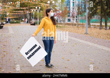 Donna mascherata che tiene un poster con testo sul russo, tradotto dal russo Stop the pandemic Foto Stock