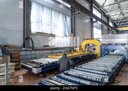 Deposito di prodotti finiti. Nastro trasportatore o linea con tegole metalliche confezionate all'interno dell'officina mediante gru. Produzione industriale di coperture su attrezzature automatizzate. Foto Stock