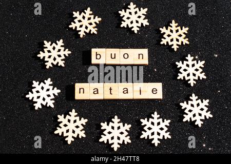 Concetto di Natale - fiocchi di neve in legno e l'iscrizione in BUONE NATALE italiano da lettere in legno su sfondo nero lucido stellato. Auto di Natale Foto Stock