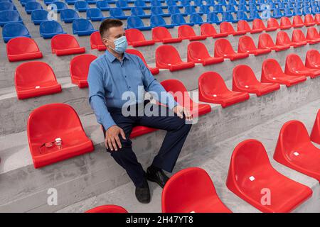 Calcio stand con sedie di plastica rossa e blu. Tifoso di calcio con maschera protettiva nello stadio. Competizioni sportive durante la quarantena e il Lockdo Foto Stock