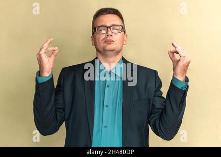 Rilassato uomo d'affari millenario in piedi meditando con gli occhi chiusi. Modello maschio in posa per fotoshoot indossare occhiali. Controllo delle emozioni, yoga, calma Foto Stock