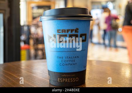 LONDRA - Oct 21: Interno del Cafe Nero. Tazza di carta con logo Nero su un tavolo. Ottobre 21. 2021 nel Regno Unito. Nero è un'azienda britannica di coffee house con sede principale Foto Stock