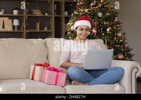 Sorridendo giovane bella indiana donna usando il computer, festeggiando il Natale. Foto Stock