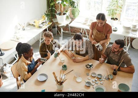 Scatto ad angolo alto del gruppo creativo della gente che decora la ceramica in officina della ceramica, spazio della copia Foto Stock