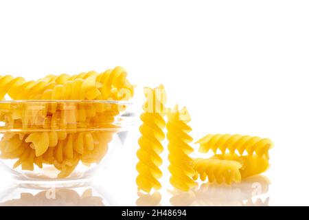 Pasta Fusilli cruda giallo brillante in un piatto di vetro, primo piano, isolata su bianco. Foto Stock