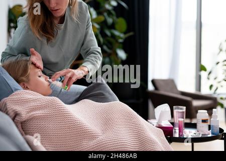 La mamma usa spray nasale per trattare il naso bloccato della figlia e tocca la fronte Foto Stock