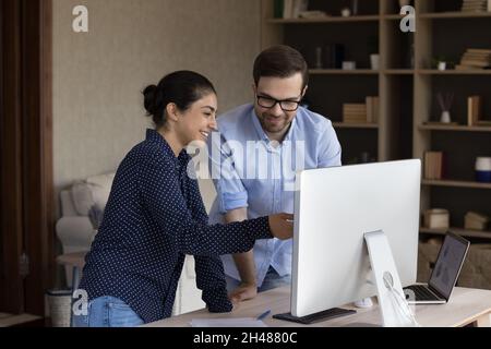 Felici giovani dipendenti di gara mista che guardano al monitor del computer. Foto Stock