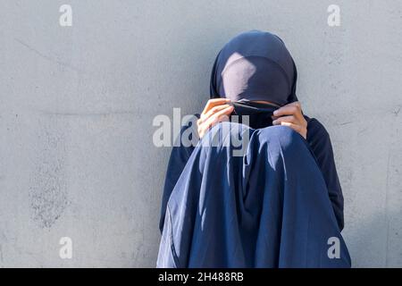 Ragazza musulmana, donna seduta in una strada della città. Povera donna musulmana con faccia chiusa che chiede elemosina. Foto Stock