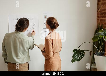 Vista posteriore a due giovani creativi progettano progetto di design a parete in studio minimale, spazio copia Foto Stock