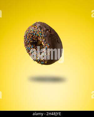 ciambelle al cioccolato con spolverette multicolore levitate su sfondo giallo Foto Stock