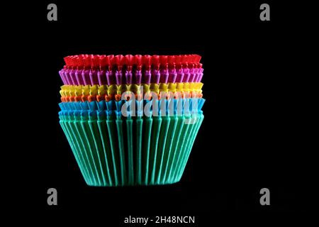 Contenitori impilati per la cottura di cupcake di carta multicolore isolati su sfondo nero Foto Stock