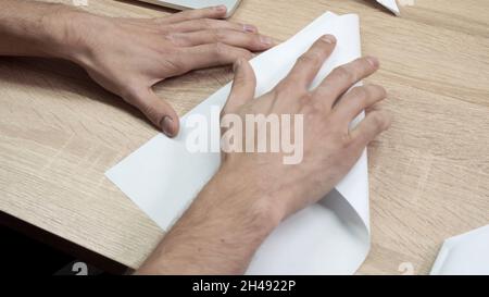 Primo piano della carta originale pieghevole. Riprese in stock. Le mani degli uomini sono piegate da carta bianca origami o aeroplano. Classe Origami durante la pausa al lavoro. Foto Stock