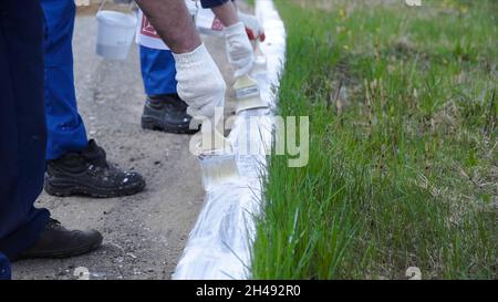 Persone che lavorano a mano indossando guanti bianchi e verniciate con una spazzola di vernice sui bordi. Clip. Lavoratori in forma dipinta. Foto Stock