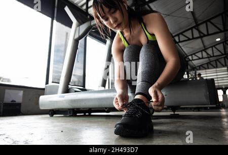 Primo piano di giovani donne asiatiche che allacciano scarpe sportive prima di esercitarsi in palestra. Foto Stock