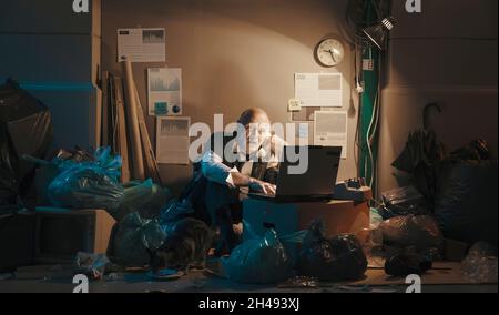 Disperato uomo d'affari rotto seduto per strada e di lavoro, sta facendo una telefonata e utilizzando un laptop, concetto di crisi finanziaria Foto Stock