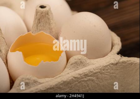 Uova di pollo bianche e un uovo rotto in un vassoio di cartone bianco, primo piano selettivo fuoco Foto Stock