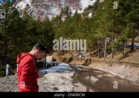 Il ragazzo lancia un quadricottero per sparare una strada di montagna serpentina. Tiro amatoriale della natura da un'altezza. Viaggiare in Georgia. Foto Stock
