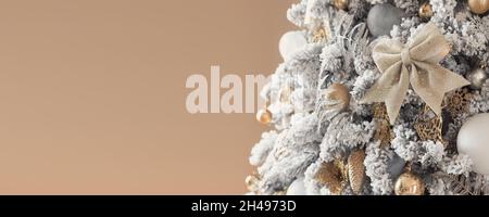 Trendy albero di natale innevato di lusso decorato in colori dorati su uno sfondo beige. Spazio di copia. Foto Stock