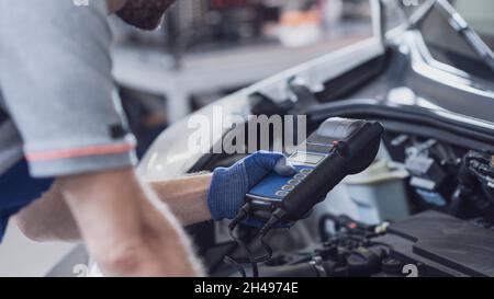 Meccanico professionista che fa un'ispezione dell'automobile, sta usando un tester della batteria Foto Stock