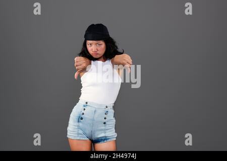 ragazza asiatica piuttosto giovane con bandana, pollici giù e disapprovando il gesto Foto Stock