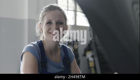 Bella meccanica femminile nel laboratorio auto, lei sta sorridendo alla macchina fotografica Foto Stock