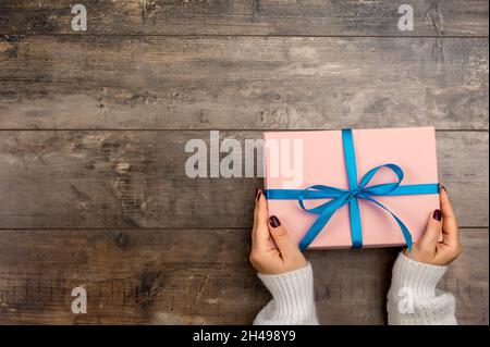 Vista ritagliata della donna che tiene avvolto regalo di natale. Donna tenere regalo di natale o di compleanno. Donna mani che tengono la scatola regalo su sfondo rustico in legno Foto Stock