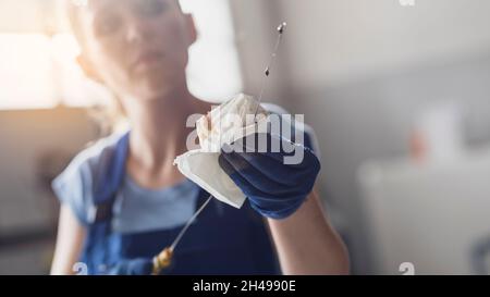 Meccanico professionale femminile che controlla l'olio motore di un'auto con un'astina di livello Foto Stock