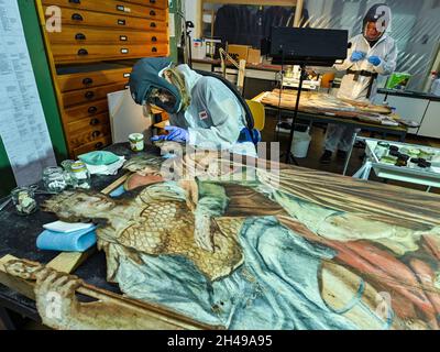 01 novembre 2021, Brandeburgo, Wünsdorf: Birgit Müller, restauratore qualificato, lavora in un vestito protettivo nel laboratorio di restauro del Landesamt für Denkmalpflege und Archäologisches Landesmuseum (BLDAM) su una pittura a figura di un teatro barocco allestito dal Monastero di Neuzelle. Grazie al generoso sostegno a lungo termine del commissario federale per la cultura e i mezzi di comunicazione (BKM), l'Ostdeutsche Sparkassensstiftung con lo Sparkasse Oder-Spree e la volontà del Ministero della scienza, della ricerca e della cultura (MWFK), l'Ufficio di Stato di Brandeburgo per la conservazione dei monumenti An Foto Stock