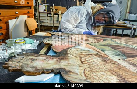 01 novembre 2021, Brandeburgo, Wünsdorf: Birgit Müller, restauratore qualificato, lavora in un vestito protettivo nel laboratorio di restauro del Landesamt für Denkmalpflege und Archäologisches Landesmuseum (BLDAM) su una pittura a figura di un teatro barocco allestito dal Monastero di Neuzelle. Grazie al generoso sostegno a lungo termine del commissario federale per la cultura e i mezzi di comunicazione (BKM), l'Ostdeutsche Sparkassensstiftung con lo Sparkasse Oder-Spree e la volontà del Ministero della scienza, della ricerca e della cultura (MWFK), l'Ufficio di Stato di Brandeburgo per la conservazione dei monumenti An Foto Stock