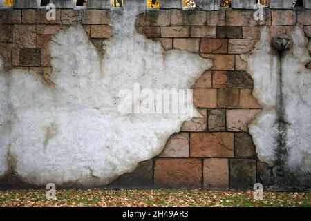 Frammento di una recinzione in pietra in stile grunge. Vecchio muro di shabby su un edificio in un parco cittadino. Muro con mattoni e frammenti di cemento, crepe e gocciolamenti Foto Stock