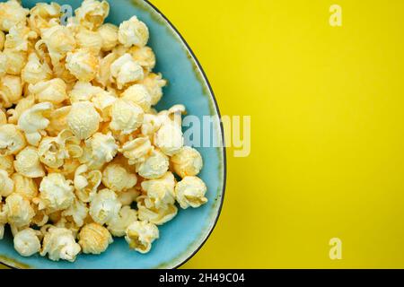 Popcorn con spezie in un piatto blu su sfondo giallo vista dall'alto. Popcorn salato con sapore di formaggio in una ciotola, luogo per il testo. Granaglie di mais da Ar Foto Stock