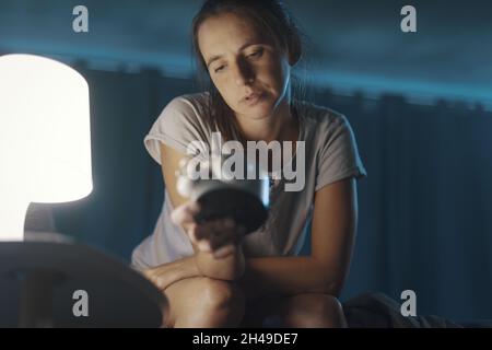 Donna insonne seduta sul letto e controllando l'ora sulla sveglia, soffre di insonnia Foto Stock