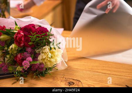 Fiorista femminile al lavoro che organizza vari fiori in bouquet, decorando bouquet. Primo piano mani di giovane donna in piedi dietro la scrivania fare bouquet di Foto Stock