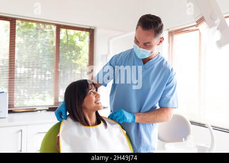 Dentista maschio caucasico che indossa maschera facciale che prepara il paziente femminile in clinica dentale moderna Foto Stock