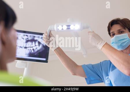 Infermiere dentale femmina caucasico che indossa maschera facciale che tiene la lampada presso la clinica dentale moderna Foto Stock