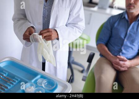 Dentista femminile biraciale che indossa guanti medici e paziente maschile in attesa presso la moderna clinica dentale Foto Stock