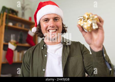 Ritratto di uomo disabile caucasico che indossa un cappello santa che tiene regalo di natale a casa Foto Stock