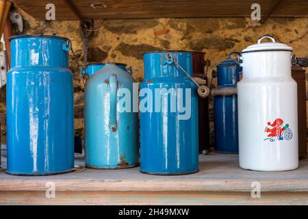 Contenitori di latte retrò blu, turchese e bianco su una mensola di legno. Foto Stock