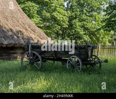 OPOLE, POLONIA - 20 giugno 2021: Un'antica carrozza di legno di fronte ad una tradizionale casa di legno, nella soleggiata giornata estiva, in un museo all'aperto. Foto Stock