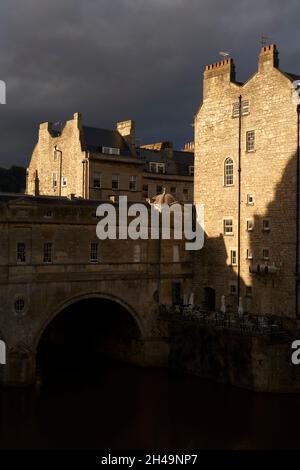 Edifici illuminati dal sole che circondano Pulteney Bridge sul fiume Avon nella storica città di Bath nel Regno Unito Foto Stock
