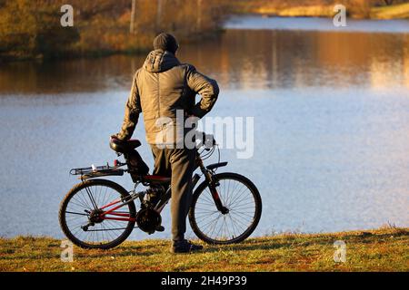 L'uomo si fermò in bicicletta sul lago e sullo sfondo della foresta autunnale. Ciclismo, viaggi e tempo libero in autunno stagione Foto Stock