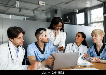 Personale medico multietnico uomini, donne di diverse età in abbigliamento da lavoro che la mattina breefing alla clinica, guardando lo schermo del notebook, prendendo appunti, avendo co Foto Stock