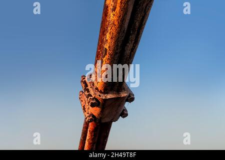 Un frammento di una fune di acciaio arrugginita nel fissaggio del ponte si estende sullo sfondo di un cielo blu Foto Stock