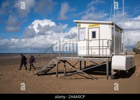 Bagnini capanna sulla spiaggia con 2 persone passeggiando oltre indossando cappotti invernali Foto Stock