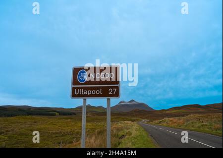 NC500 Firma con chilometraggio a Ullapool. Strada a lato e sfocato paesaggio di montagna sullo sfondo. Cielo blu con nuvole, un sacco di spazio di copia. Foto Stock