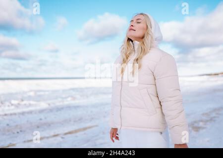 Donna che indossa abiti bianchi sente il freddo sulla costa invernale del mare. Le donne respirano con aria fresca camminando lungo il mare o la spiaggia dell'oceano. Foto Stock