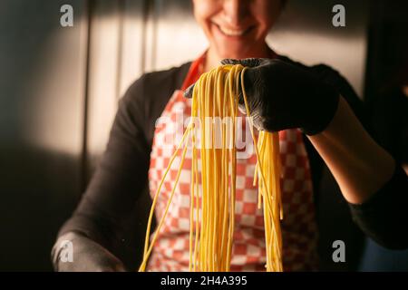 Le mani femminili fanno la pasta nell'aria, polverulente dalla farina. Stile scuro a contrasto con il suo sorriso Foto Stock
