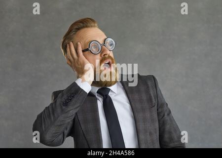 Divertente sorpreso uomo d'affari in occhiali rotondi guardando via con espressione del volto scioccato Foto Stock