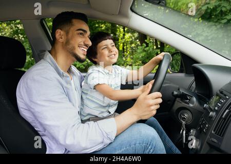 Carino ragazzo piccolo e il suo giovane padre arabo che Riding Car insieme, bambino piccolo maschio seduto sul papà Lap in Automobile, Caring Medio Oriente Daddy Teach Foto Stock